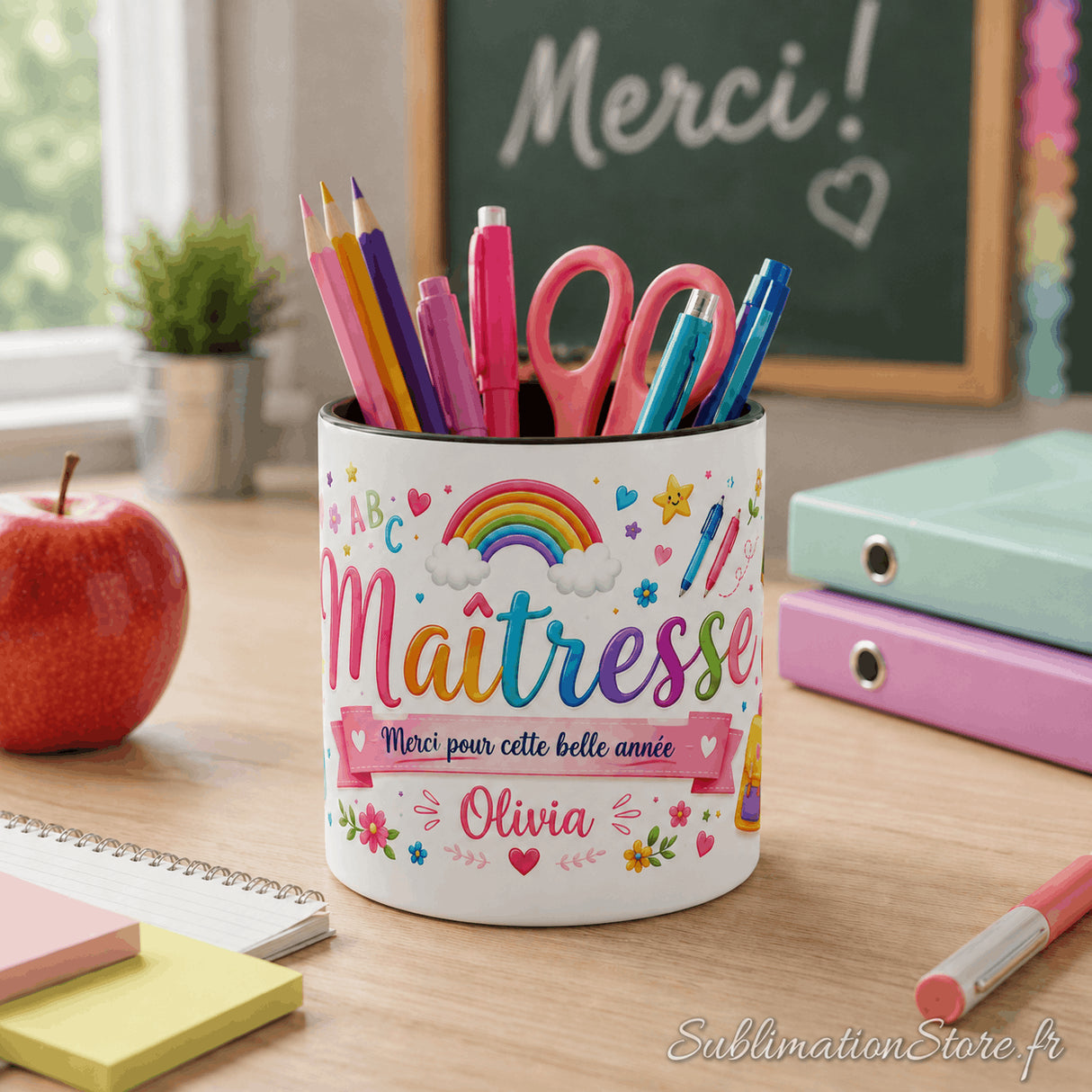 Pot à crayons maîtresse personnalisé sur bureau de classe devant tableau avec inscription Merci