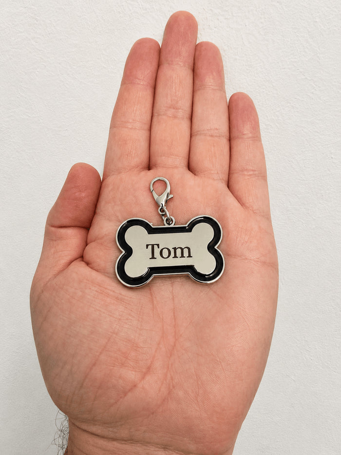 Médaille chien personnalisée en forme d'os avec le prénom Tom gravé au laser, tenue dans une main, fabriquée par SublimationStore