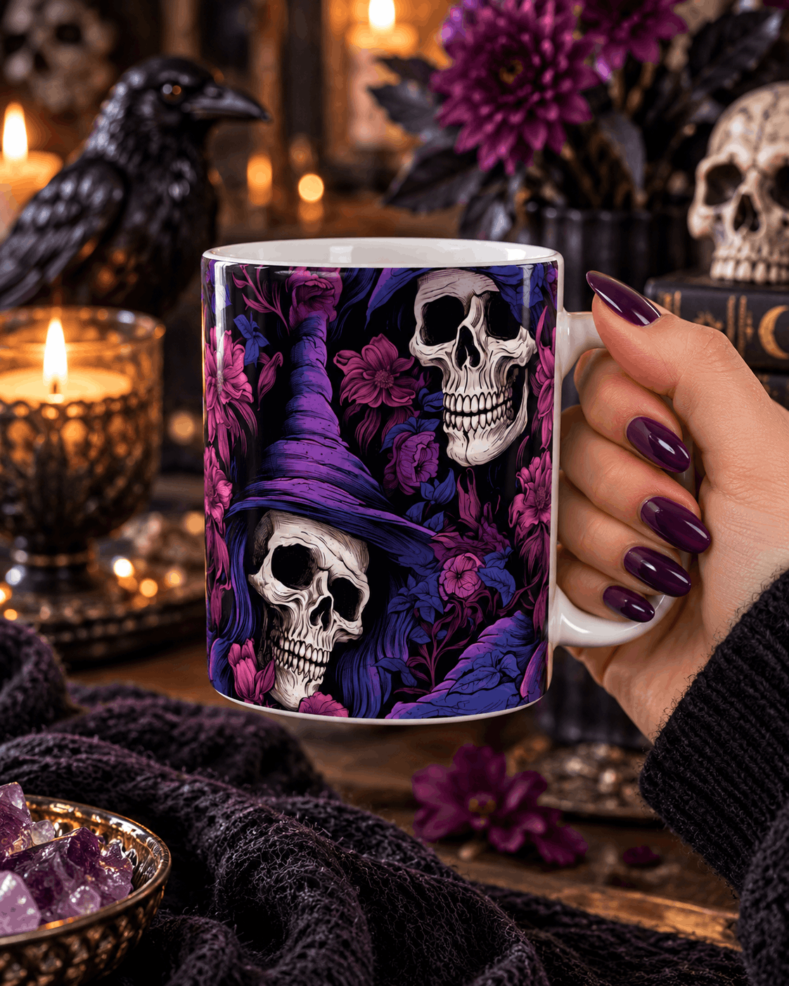 Main tenant le mug crâne sorcière et fleurs violettes, décor gothique avec corbeau, bougies, améthystes et grimoire