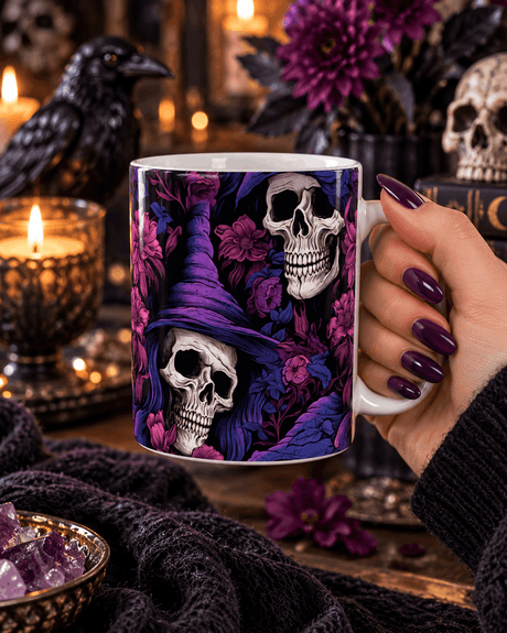 Main tenant le mug crâne sorcière et fleurs violettes, décor gothique avec corbeau, bougies, améthystes et grimoire