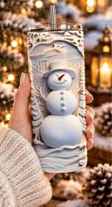 Tumbler bonhomme de neige tenu dans la main, avec pull en maille et lanterne allumée en arrière-plan